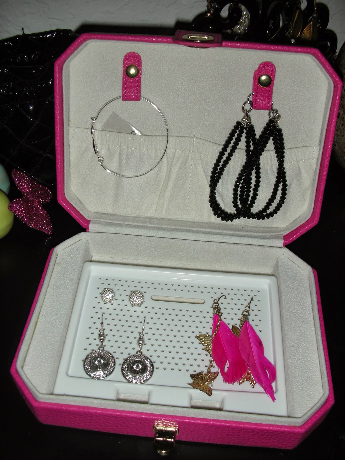 An open pink jewelry box displaying earrings, a bracelet, and a bangle, bright and organized mood.